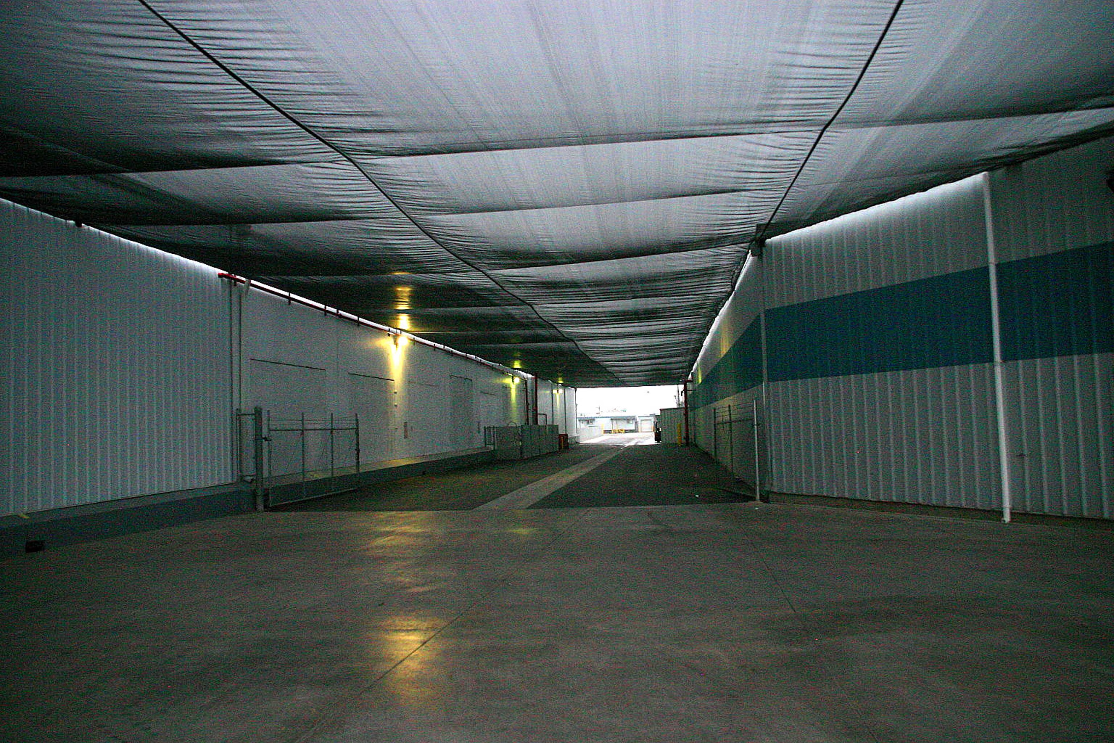 Interior of packing and storage facility with 80% shade net covering long corridor between corrugated metal walls
